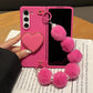 Pink phone case with heart design and pom-pom keychain on a wooden surface.