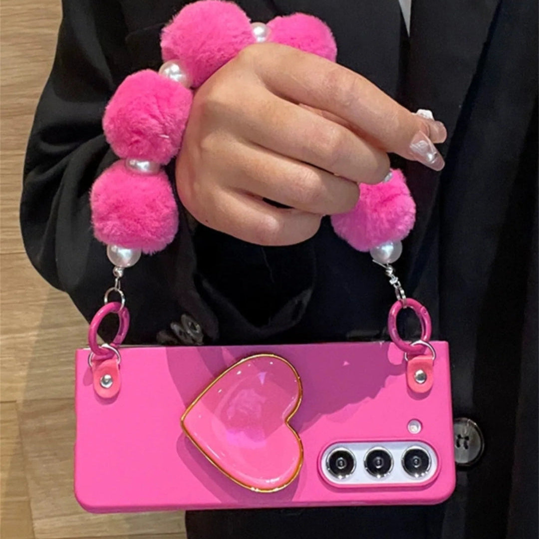 Pink phone case with heart design and pom-pom chain held by a person.