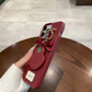 Red phone case with bow and ring holder held by a hand on a wooden table.