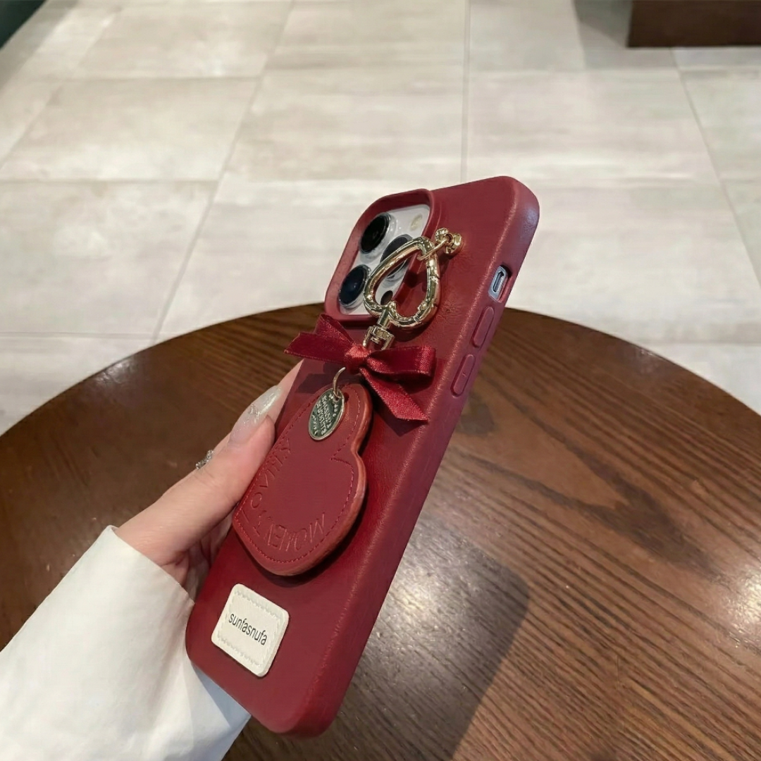 Red phone case with bow and ring holder held by a hand on a wooden table.