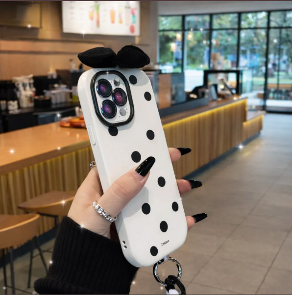 Person holding a phone case with polka dots and a bow in a cafe setting